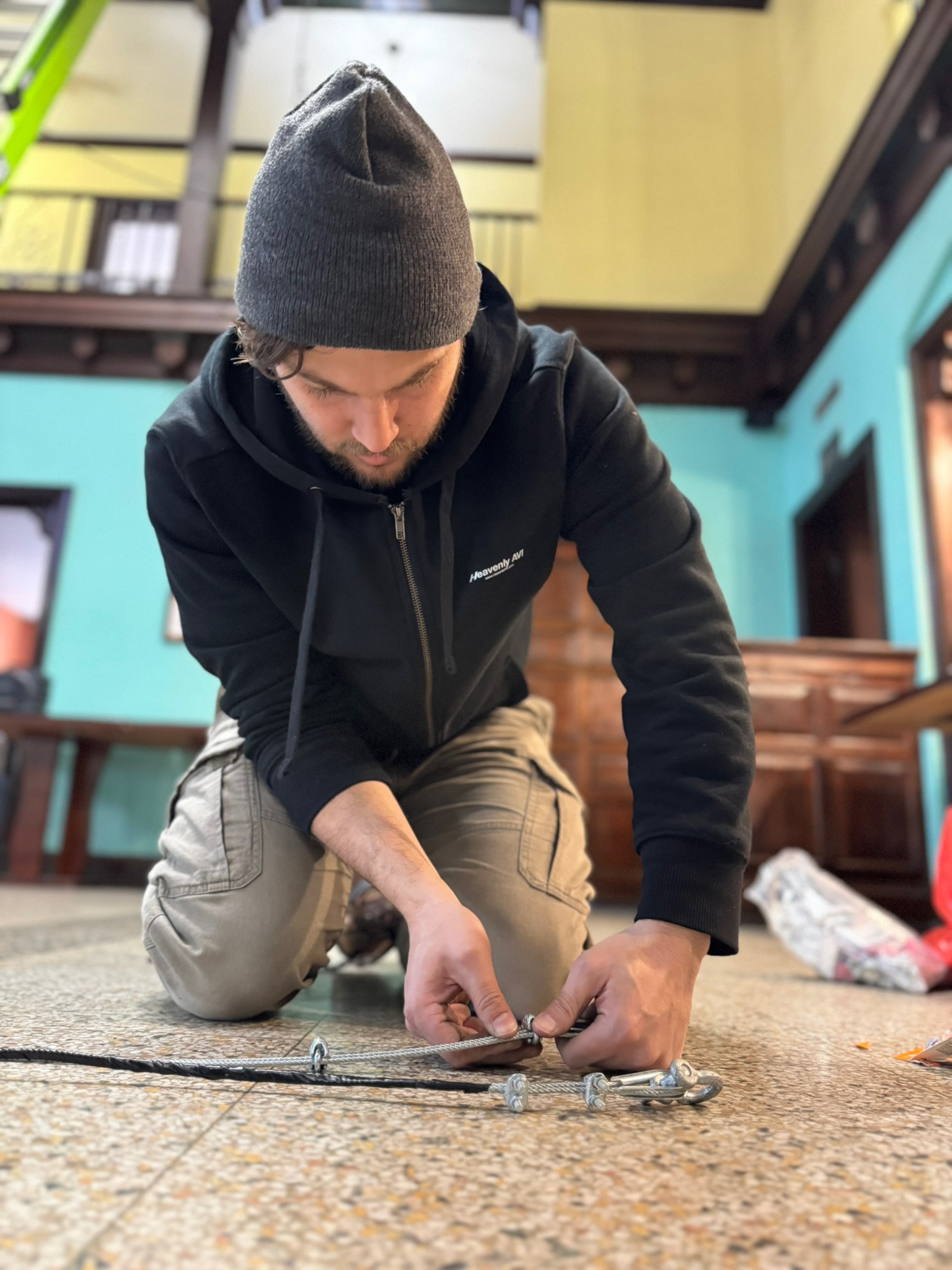 Technician kneeling and securing rigging hardware on the floor inside the worship space