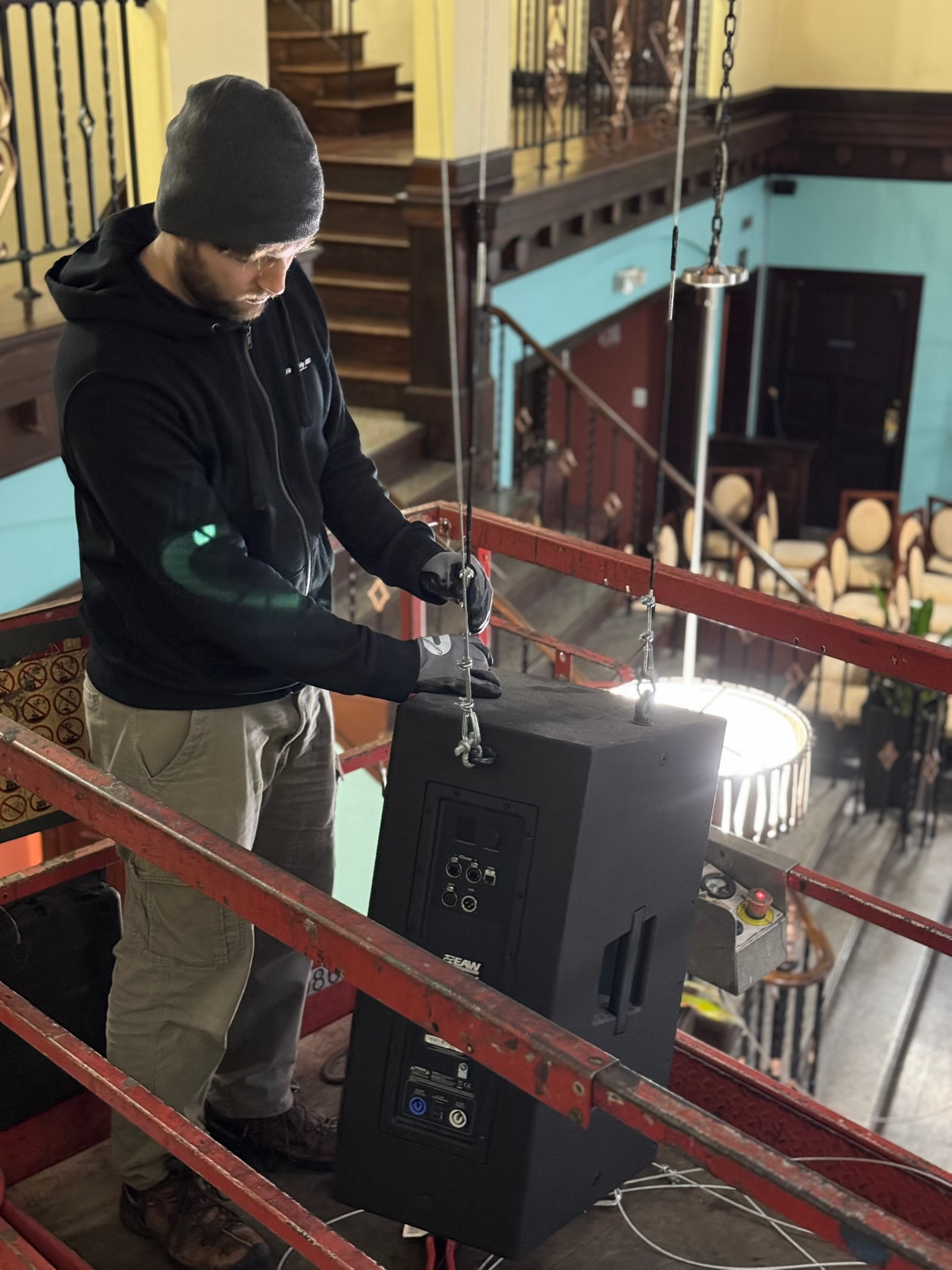 Technician on a lift adjusting and securing a hanging speaker above the room