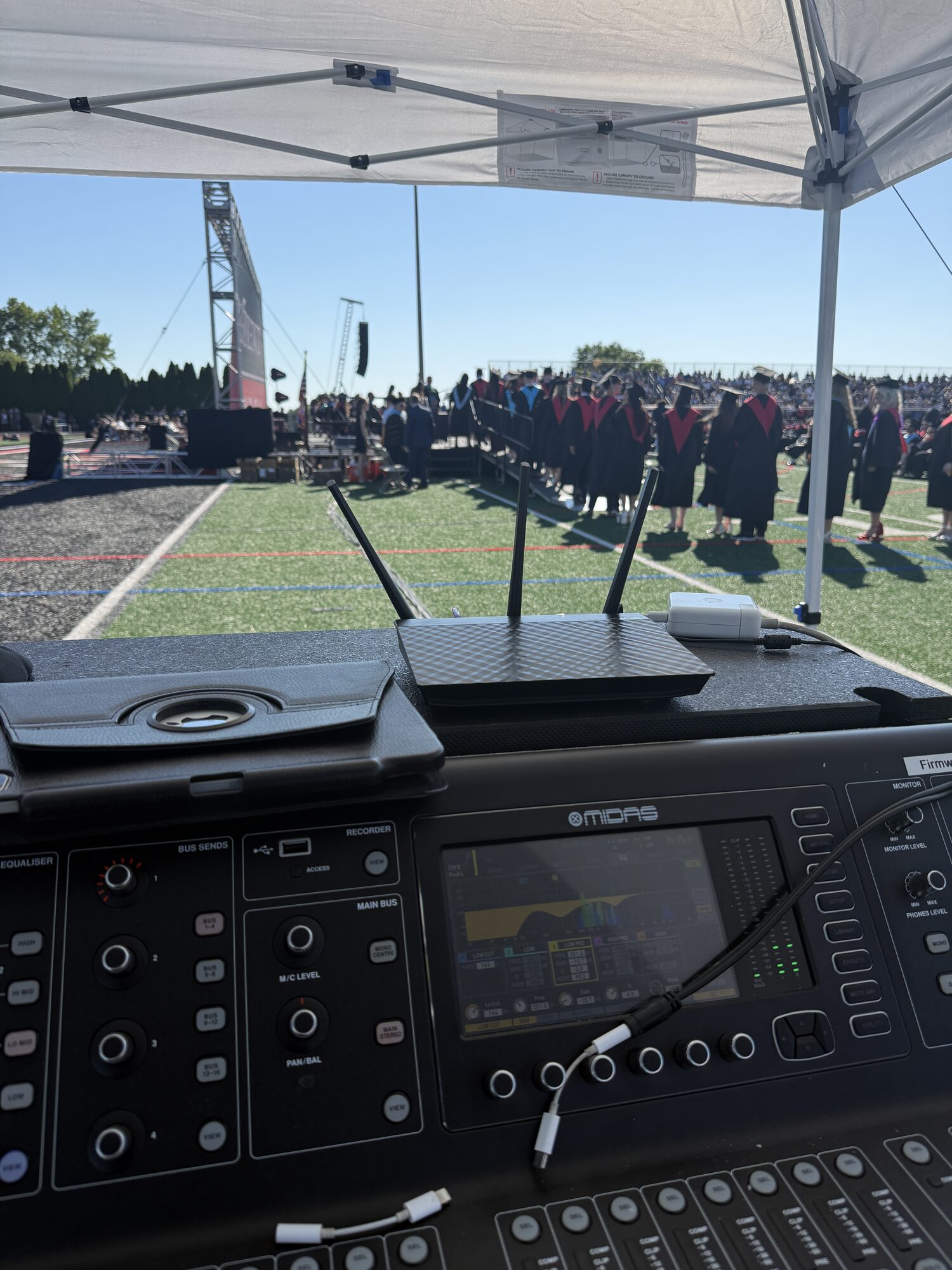 Graduates assembled on an athletic field beyond the ceremony audio position