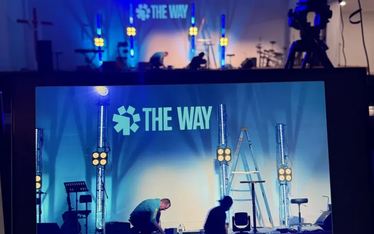 Camera and production monitor facing The Way Church stage with blue lighting and the church logo