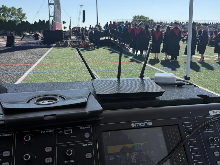 Graduates assembled on an athletic field beyond the ceremony audio position