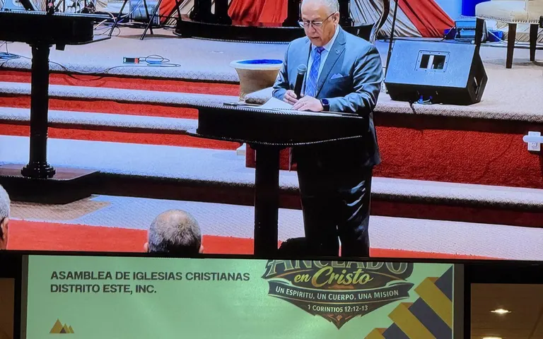 Convention speaker at the pulpit with event program screens visible in the church auditorium