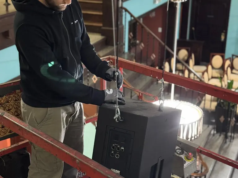 Technician on a lift adjusting and securing a hanging speaker above the room