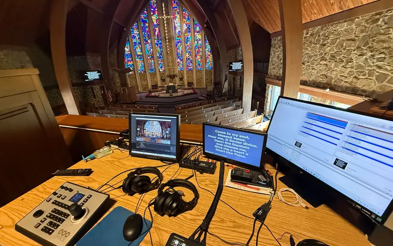Church sanctuary viewed from a video control desk with monitors, a PTZ controller, and a switcher