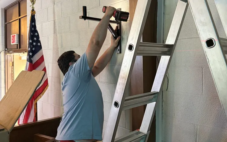 Technician mounting a display bracket on a church wall during installation work