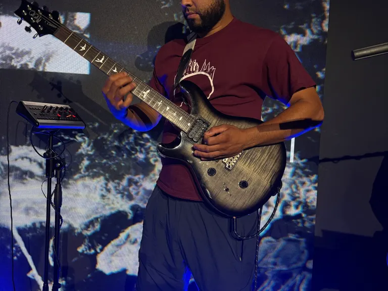 Electric guitarist performing in front of a large LED wall with blue floor lighting